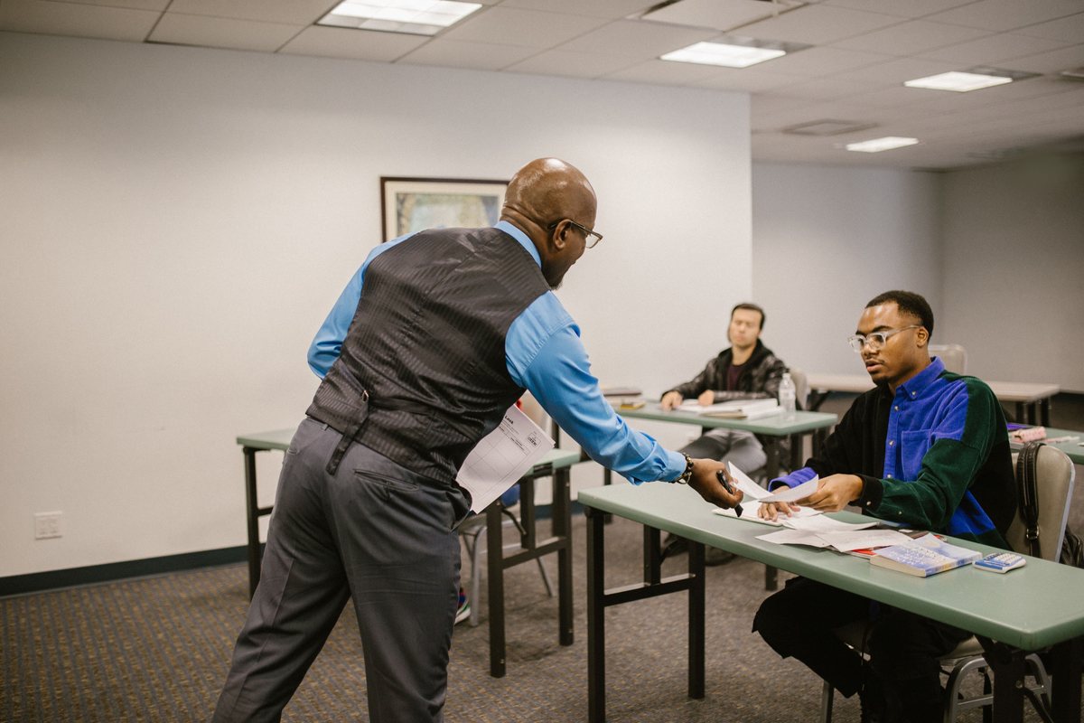A teacher handing a paper to an adult student in a classroom