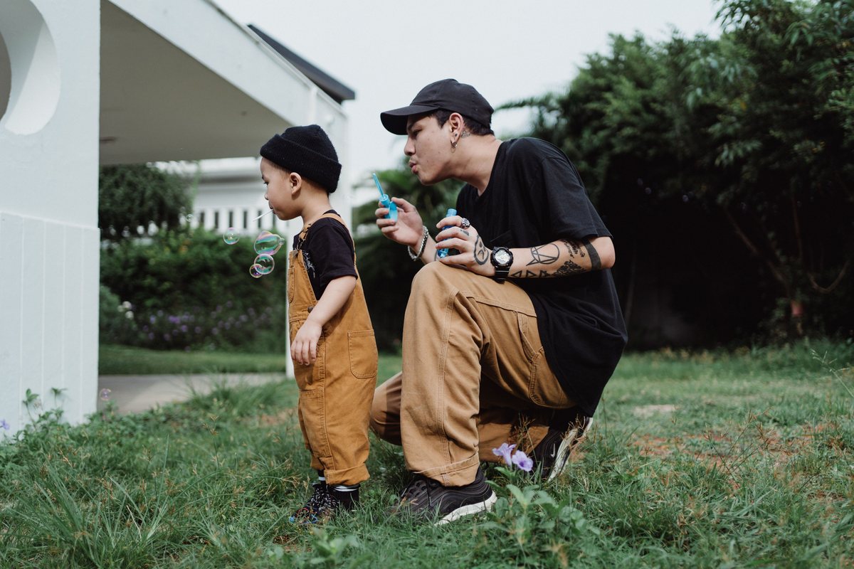 A father crouched beside his young son in a yard